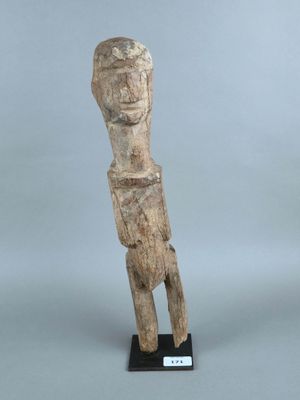 une vieille statue en bois représentant un homme, posée sur un socle noir