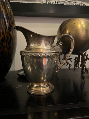 a silver pitcher sitting on top of a table next to a vase