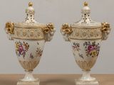 two white vases with gold trim and flowers on them sitting on a table