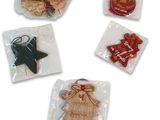 quatre décorations de Noël dans des sachets, posées sur une surface blanche