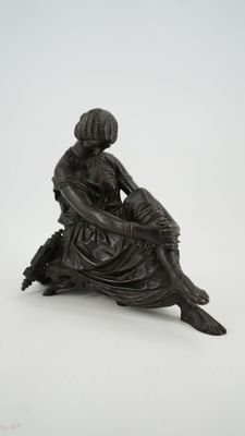 an antique bronze figurine of a woman sitting on a tree stump
