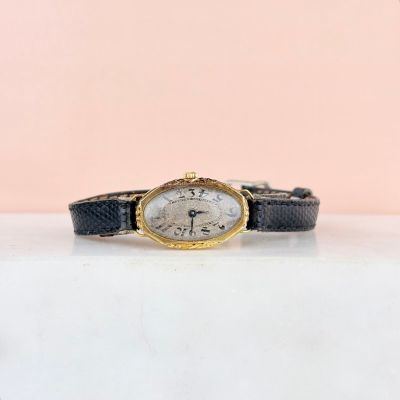 un gros plan d'une montre posée sur une table, sur fond rose