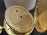 une montre de poche en or posée à côté d'un récipient blanc