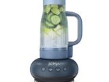 a blue blender with cucumbers in it on a white surface