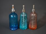three different colored glass bottles are lined up on a gray surface