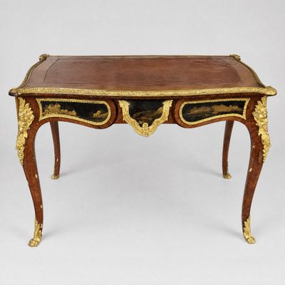 an antique writing table with a gold leaf decoration and a brown leather top