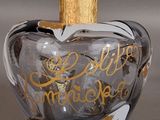 an apple shaped glass bottle with gold writing on it