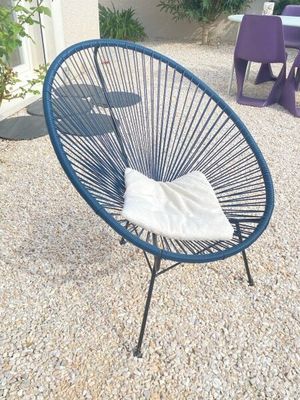 une chaise bleue posée sur un sol en gravier, à côté d'une table et de chaises