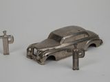 une petite voiture argentée et une clé posées sur une surface blanche