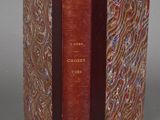 an old book with a red cover sitting on top of a table