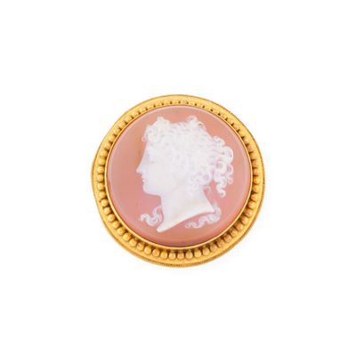 un gros plan sur une broche rose et dorée représentant le profil d'une femme