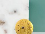 broche plaquée or ornée de pierres noires et blanches sur un fond en marbre