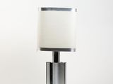 une lampe de table argentée surmontée d'un abat-jour blanc