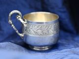 an antique silver cup with a handle on a blue cloth