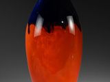 un vase orange et bleu posé sur une surface blanche