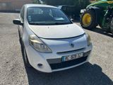 une petite voiture blanche garée sur un parking, avec un tracteur derrière elle