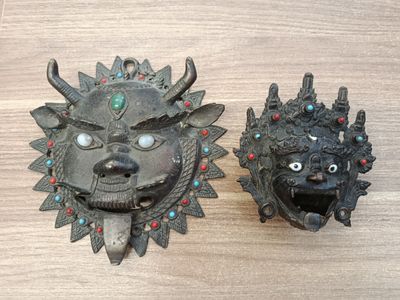 pair of metal masks on a wooden table with red and blue beads