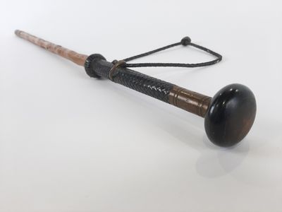 une vieille batte de baseball avec un manche en bois, posée sur une surface blanche