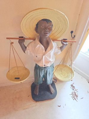 une statue représentant un garçon coiffé d'un chapeau de paille et tenant une balance