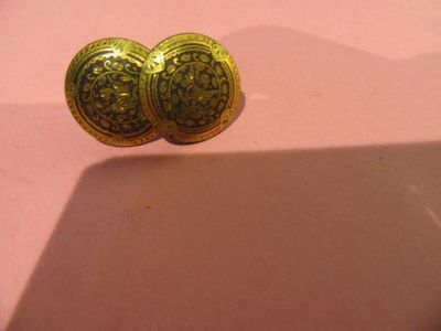 une paire de boutons dorés posés sur une surface rose