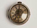 une montre de poche en argent posée sur une surface blanche, sur fond blanc