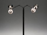 a pair of silver plated earrings on a black stand