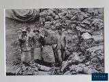 a black and white photo of a group of men standing in front of a pile of bags