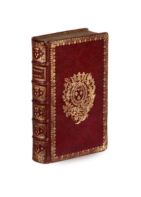 an old red book with gold trim sitting on top of a white surface