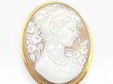 an image of a woman ' s profile is shown in a white and gold broochle