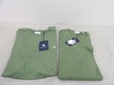 two green t - shirts with tags on them sitting on a white surface