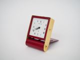 a small red clock sitting on top of a wooden stand