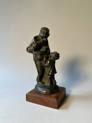 figurine en bronze représentant un homme tenant un enfant dans ses bras, posée sur un socle en bois