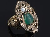 gros plan d'une bague en or avec une pierre verte et des diamants