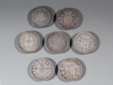six pièces d'argent sont disposées en triangle sur une surface blanche