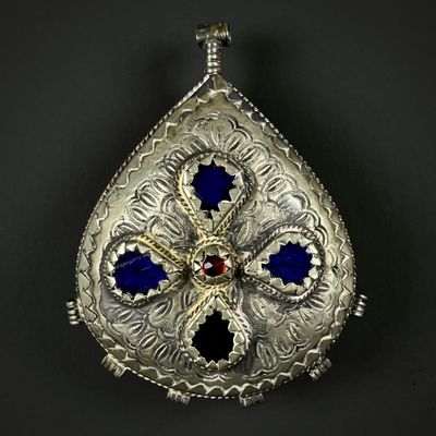 un pendentif en argent richement orné, avec des pierres bleues et rouges sur fond noir