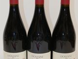 trois bouteilles de vin rouge sont alignées sur une surface blanche
