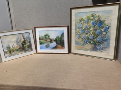 three framed paintings of flowers on a table next to a wall