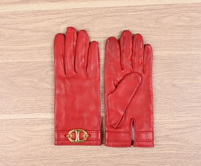 des gants en cuir rouge ornés de boucles dorées, posés sur un parquet