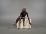 statue of a man sitting on a block with his hands on his knees