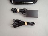 a black game console with a charger and a power cord