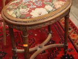 a small wooden stool with a floral seat on a red rug