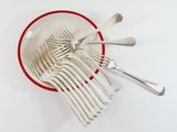 a lot of forks in a red bowl on a white table