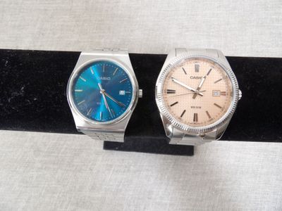 two watches are sitting on a black stand on a white surface