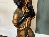 gold and black statue of a woman holding a pot on a wooden floor