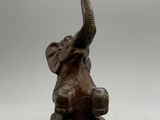 une statue d'éléphant assis par terre, la trompe levée