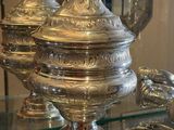 une table en verre sur laquelle sont disposés des plats en argent, avec une lampe en arrière-plan