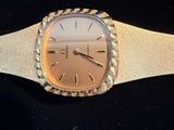an image of a gold watch with a white band on a black surface