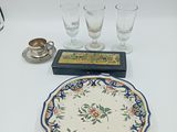 a plate with a flower design on it next to four glasses and a candle holder