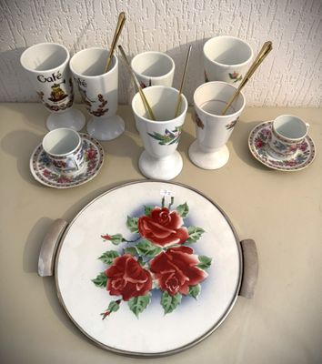 une assiette blanche ornée de roses rouges, à côté de tasses et de cuillères