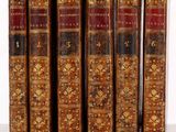 Six vieux livres sont alignés sur une étagère devant un fond blanc.